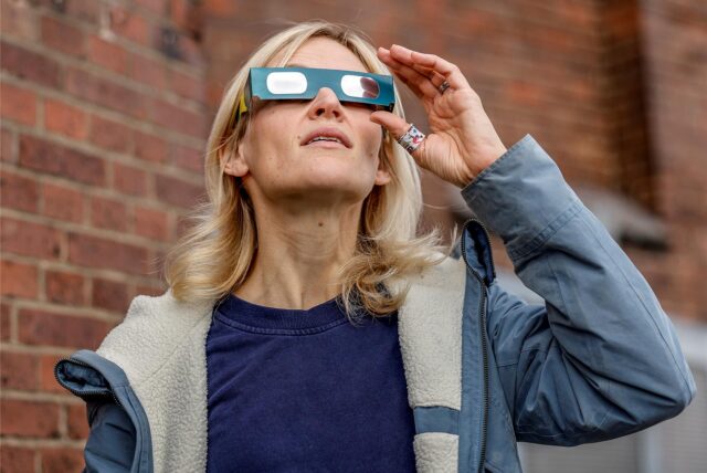 Eine Frau trägt eine Schutzbrille und blickt zum Himmel, um eine partielle Sonnenfinsternis zu beobachten.