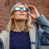 Eine Frau trägt eine Schutzbrille und blickt zum Himmel, um eine partielle Sonnenfinsternis zu beobachten.