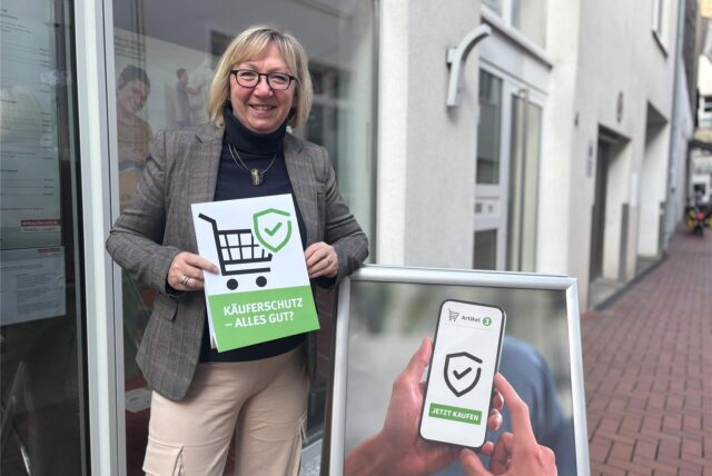 Rose Sommer steht vor der Verbraucherzentrale in Castrop-Rauxel und hält ein Schild auch auf dem steht: „Käuferschutz-Alles gut?“.
