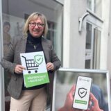 Rose Sommer steht vor der Verbraucherzentrale in Castrop-Rauxel und hält ein Schild auch auf dem steht: „Käuferschutz-Alles gut?“.