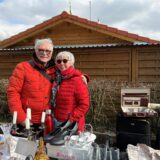 Ein Paar hinter einem Trödelmarkt-Stand mit verschiedenen Dingen aus dem Haushalt.