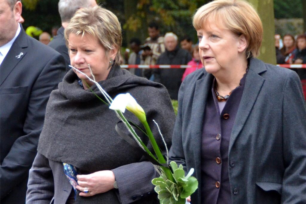 Sylvia Löhrmann begleitet Angela Merkel zur Gedenkstätte in Haltern, in der Hand halten sie weiße Kalla.