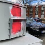 Unbekannte haben den Panzerblitzer an der Scherlebecker Straße in Herten mit roter Farbe beschmiert. Ein schwarzer BMW fährt in diesem Moment vorbei.