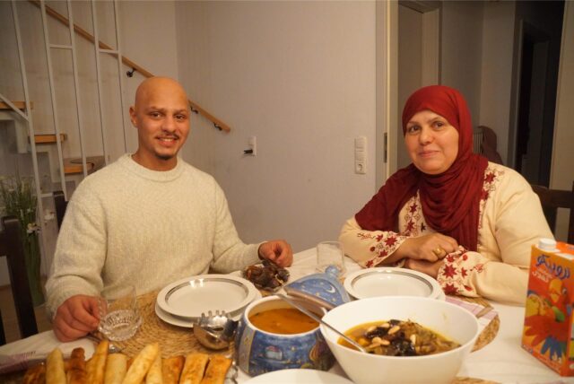 Ein junger Mann und eine Frau mit Kopftuch sitzen an einem gedeckten Tisch.