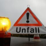 Ein Warnschild mit der Aufschrift „Unfall“ und eine Signalleuchte stehen auf einer Fahrbahn.