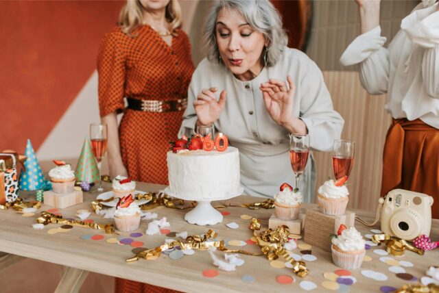 Eine Frau pustet die Kerzen auf einem Kuchen zum 60. Geburtstag aus.