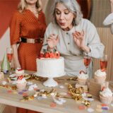 Eine Frau pustet die Kerzen auf einem Kuchen zum 60. Geburtstag aus.