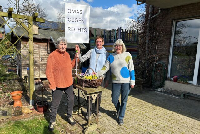 Diederika Forster, Ursula Münzner und Gudrun Güth stehen im Garten und halten ein Plakat mit der Aufschrift „Omas gegen Rechts“ hoch.