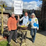 Diederika Forster, Ursula Münzner und Gudrun Güth stehen im Garten und halten ein Plakat mit der Aufschrift „Omas gegen Rechts“ hoch.
