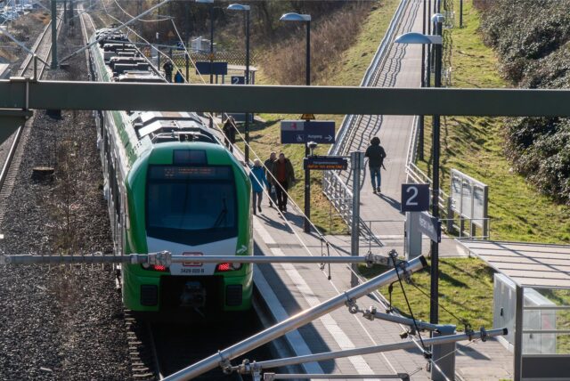 Das Bild zeigt den Haltepunkt Herten. Auf dem Gleis steht die S-Bahn der Linie S9. Mehrere Menschen laufen am Gleis entlang.