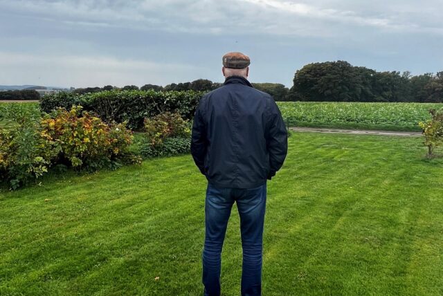 Der Polizist Stefan K. steht mit dem Rücken zur Kamera in einem Garten und blickt in die Natur.
