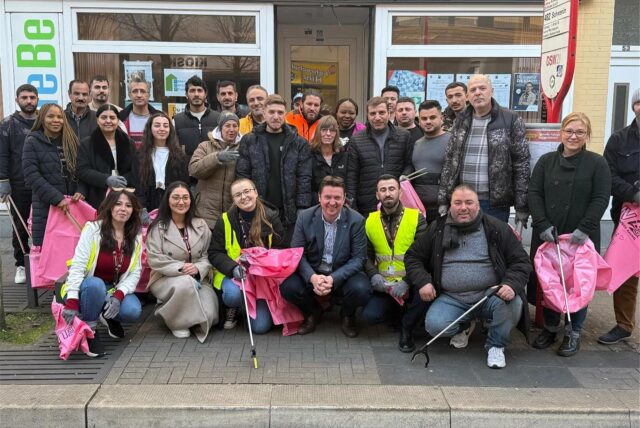 Eine Gruppe von Menschen steht mit pinken Plastikbeuteln und Greifzangen vor einem Geschäft.