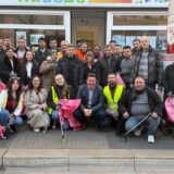 Eine Gruppe von Menschen steht mit pinken Plastikbeuteln und Greifzangen vor einem Geschäft.