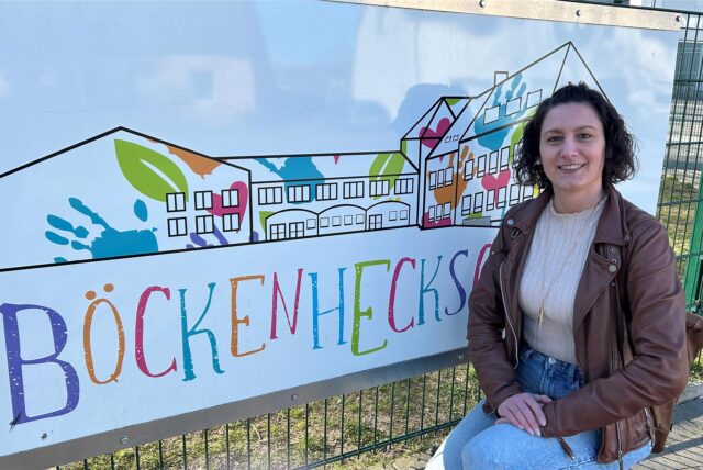 Janna Baierle sitzt in der Hocke vor einem Schild mit der Aufschrift Böckenheckschule.