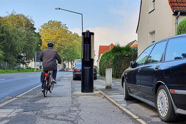 Ein Radfahrer fährt an einer Radarsäule in Herten vorbei, daneben steht ein parkendes Auto.