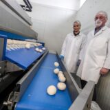Daniela und Peter Schultze aus der Geschäftsführung von Point of Food Lebensmittelvertriebs GmbH in Recklinghausen stehen an einem Produktionsband auf dem Pizzateiglinge liegen.