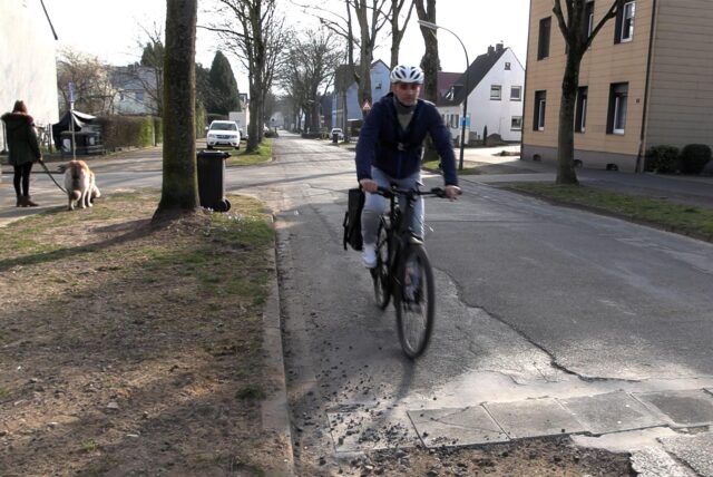 Der Reporter fährt auf seinem Fahrrad über ein Schlagloch.