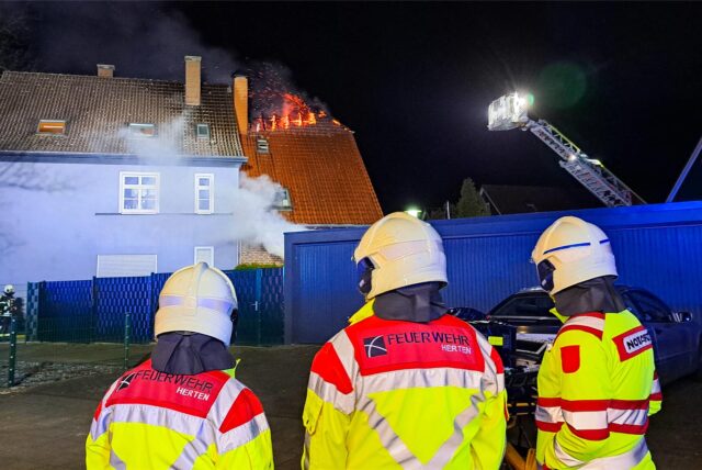 Hertener Feuerwehrmänner stehen vor dem brennenden Dachstuhl an der Feldstraße in Herten-Langenbochum.
