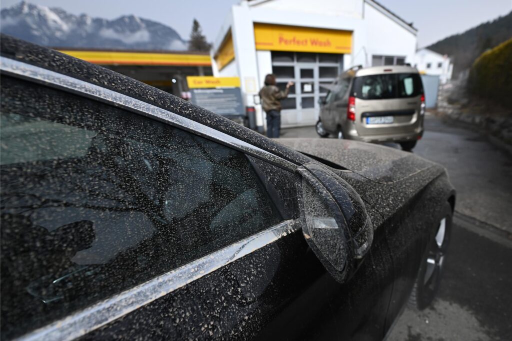 Mit Saharastaub bedeckte Autos stehen an einer Waschanlage an. Mit Saharastaub bedeckte Autos stehen an einer Waschanlage an.