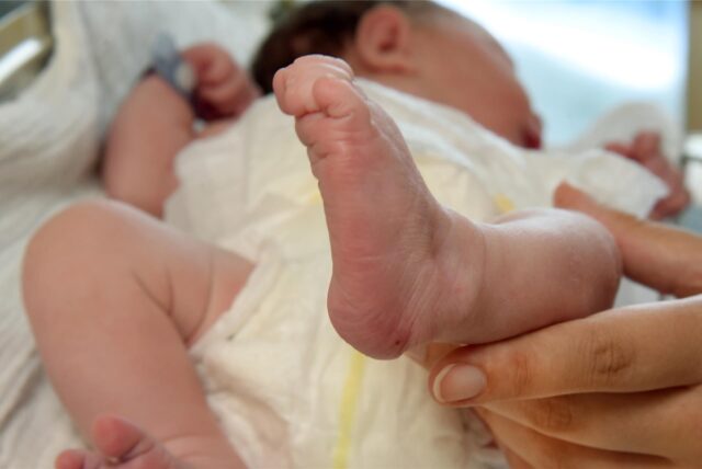 Ein schlafendes Baby, dessen Beinchen eine Frauenhand streichelt.