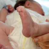 Ein schlafendes Baby, dessen Beinchen eine Frauenhand streichelt.