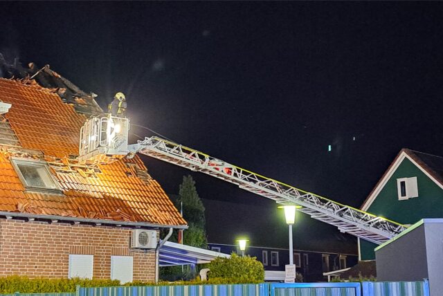 Ein Feuerwehrmann der Hertener Feuerwehr steht im Korb einer ausgefahrenen Drehleiter und blickt auf ein zerstörtes Hausdach.