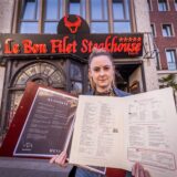 Reporterin Julia Segantini hält jeweils eine Speisekarte des Pfefferkorns und des Le Bon Filet vor dem Restaurant Le Bon Filet am Hohen Wall in Dortmund aufgeschlagen in der Hand.
