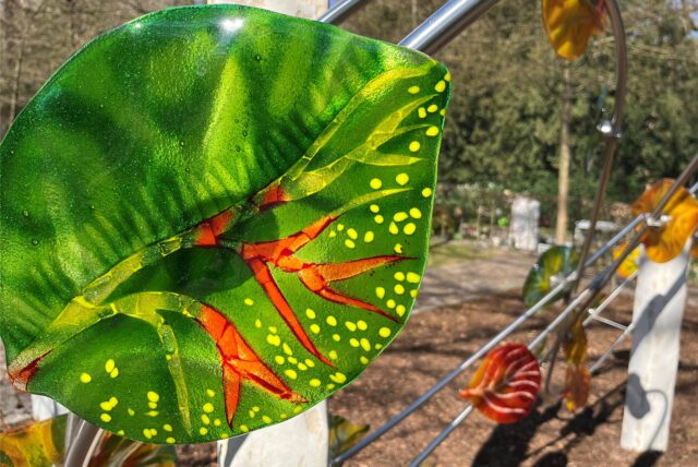 Bunte Blätter aus Glas sind an Edelstahlrohren befestigt.