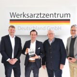 Vertreter der Stadt Recklinghausen stehen mit Jan Felix Hübner in den Räumlichkeiten der Werksarztzentrum Deutschland GmbH.