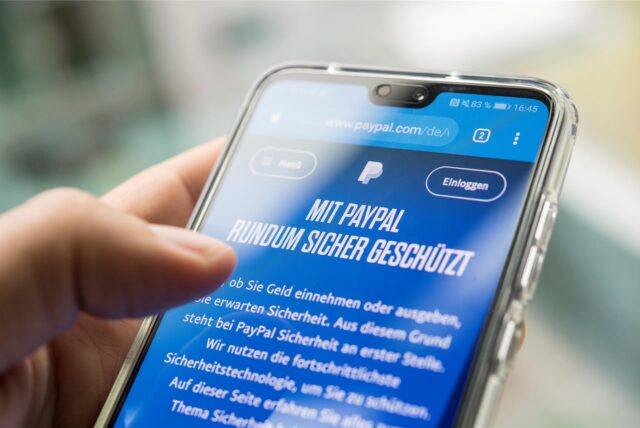 Jemand hält ein Handy, auf dem das PayPal-Logo zu sehen ist, in der Hand.