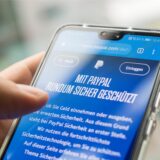 Jemand hält ein Handy, auf dem das PayPal-Logo zu sehen ist, in der Hand.