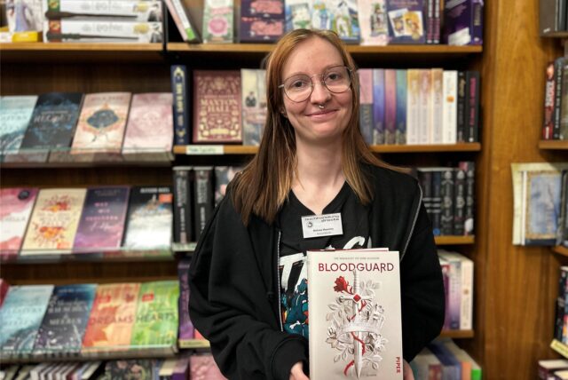 Melissa Moschny ist Auszubildende in der Buchhandlung Droste in Herten-Mitte. Sie steht vor einem Regal und hält das Buch Bloodguard in den Händen.