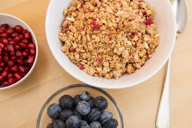 Eine Schüssel Früchtemüsli steht mit weiteren Schalen mit Obst auf einem Tisch.