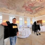 Markus Liptow, Gastronom im Schloss Herten, steht im Speisesaal. Hinter ihm in weiß eingedeckte Tische und ein Stuhlwagen für den Aufbau der Bestuhlung.