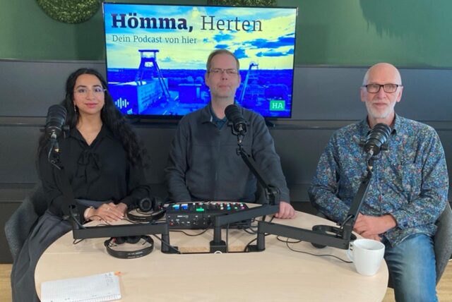 Rosi Taslima Azam, Stefan Korte und Joachim Schmidt sitzen an einem Tisch, vor ihnen Mikrofone und ein Mischpult.