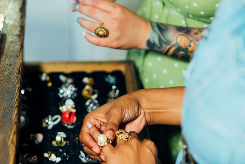 Zwei Frauen stehen auf einem Trödelmarkt in NRW vor einem Stand mit Schmuck und probieren Ringe am Zwei Frauen stehen auf einem Trödelmarkt in NRW vor einem Stand mit Schmuck und probieren Ringe am