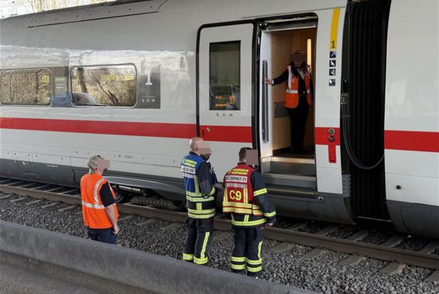 Einsatzkräfte der Feuerwehr stehen neben einem Zugabteil des ICEs, der in Dortmund auf offener Strecke evakuiert werden musste.