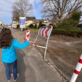 Westerholterin mit blauer Jacke und langen Haaren steht mit der Geste des Unverständnisses vor dem verbogenen Schild.