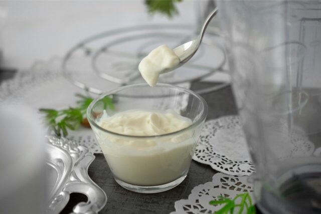 Ein Löffel mit Mayonnaise über einer Glasschale mit demselben Inhalt.