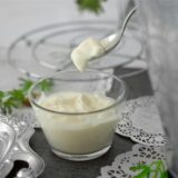 Ein Löffel mit Mayonnaise über einer Glasschale mit demselben Inhalt.