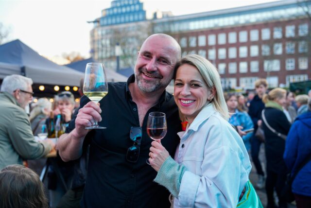 Zwei Besucher halten beim ersten Feierabendmarkt 2025 in Dortmund ein Glas Wein in der Hand.