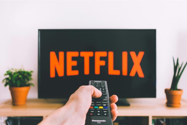 Ein Fernseher wird mit einer Fernbedienung angeschaltet und es ist das Netflix-Logo zu sehen.