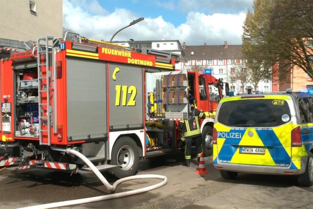 Feuerwehr und Polizei stehen auf der Tiefe Straße in Dortmund wegen eines Wohnungsbrandes.