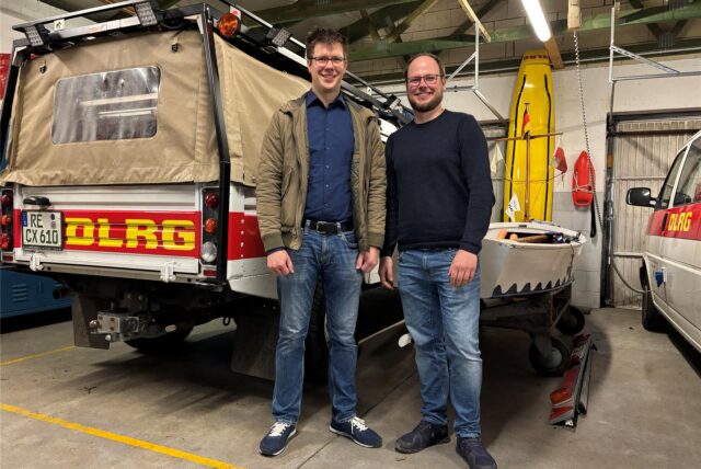 Zwei Mitglieder des DLRG Marl stehen in einer Garage neben einem Einsatzfahrzeug.