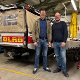 Zwei Mitglieder des DLRG Marl stehen in einer Garage neben einem Einsatzfahrzeug.