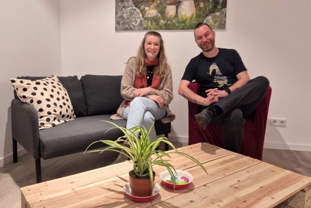 Eine Frau sitzt auf einer Couch, ein Mann sitzt daneben auf einem Sessel