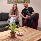 Eine Frau sitzt auf einer Couch, ein Mann sitzt daneben auf einem Sessel