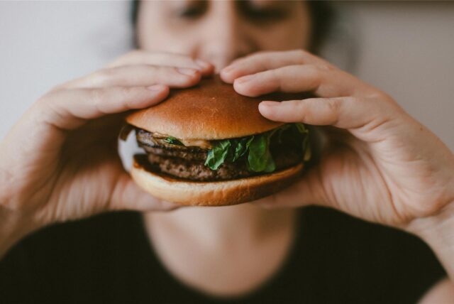 Eine Frau hält einen Burger vor ihrem Gesicht.