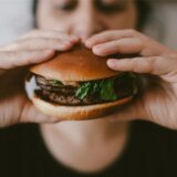 Eine Frau hält einen Burger vor ihrem Gesicht.