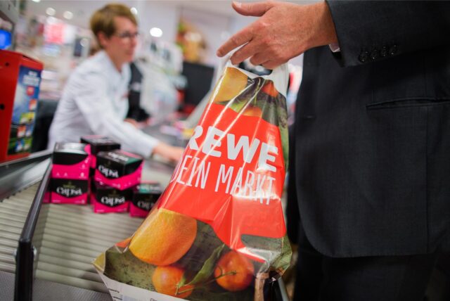 Ein Kunde packt an der Kasse eines Rewe-Marktes seine Einkäufe in eine Tragetasche aus Plastik.